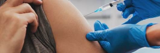 Man receiving a vaccination in left arm by nurse in teal blue surgical gloves